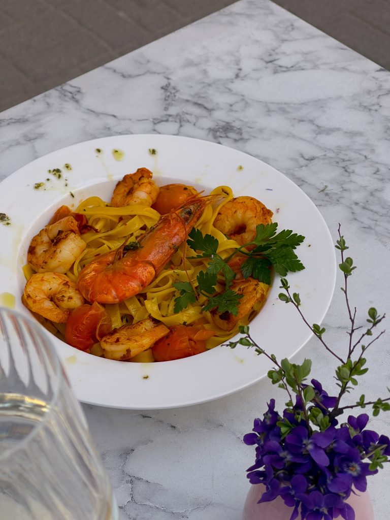 Talerz świeżego makaronu z dużymi krewetkami i pomidorkami koktajlowymi serwowany na zewnątrz w Bube Restauracja i Pizza we Wrocławiu.